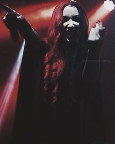 a woman with long red hair wearing a black mask and holding her hand up in the air