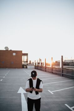 a man standing in an empty parking lot looking at his cell phone while the sun is setting