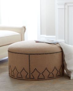 a round ottoman sitting on top of a floor next to a window