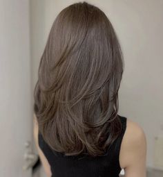 the back of a woman's head with long, brown hair in front of a mirror