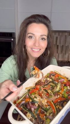 a woman holding up a casserole dish with vegetables in it and smiling at the camera