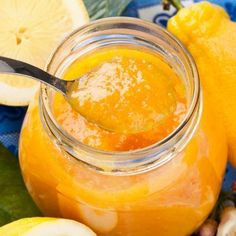 a jar filled with orange sauce next to sliced lemons and nuts on a table