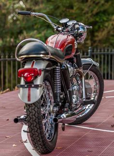 a red and black motorcycle parked in a parking lot next to a metal fence with trees behind it