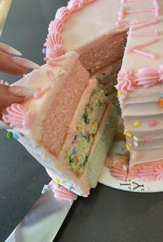 a woman is cutting into a cake with pink frosting and sprinkles