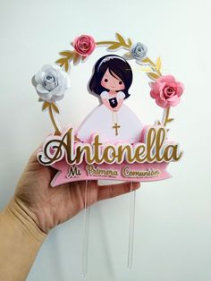 a hand holding up a cake topper that says antonioella