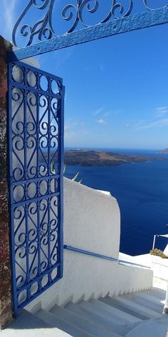 an open door on the side of a building with stairs leading up to it and blue water in the background