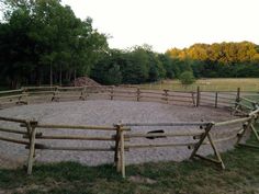 a fenced in area with an empty horse paddock on the grass and trees behind it