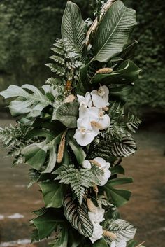 white flowers and greenery are hanging from the side of a wooden pole in front of a river