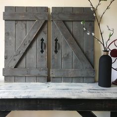 two wooden doors sitting on top of a table next to a vase with flowers in it