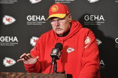 an older man in a red hoodie speaks into a microphone at a press conference