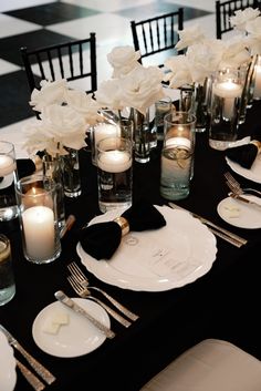 a table set with black and white place settings, silverware, candles and flowers