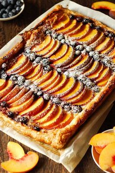 an apple tart with powdered sugar on top sits on a table next to sliced peaches