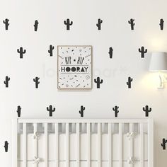 a white crib in front of a wall with black cactus decals