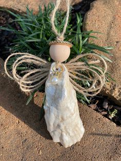 an angel statue is sitting on the ground next to some grass and rocks, with a small egg in it's back end