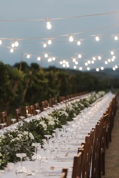 a long table with white flowers and greenery is set up for an outdoor dinner