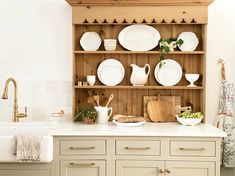 a wooden shelf filled with white plates and other kitchen ware on top of a counter