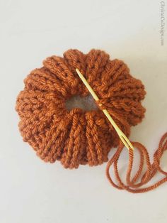 an orange ball of yarn with a crochet hook in the middle, on a white surface