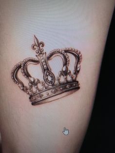 a small crown tattoo on the side of a woman's thigh, with an arrow