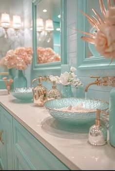 a bathroom with blue cabinets and white counter tops, gold faucets and pink flowers