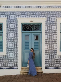 a woman standing in front of a blue and white building with shutters on the doors