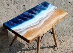 a small wooden table sitting on top of a sandy beach covered in blue and white waves