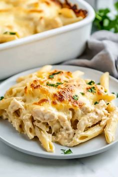 a white plate topped with pasta and chicken casserole next to a baking dish