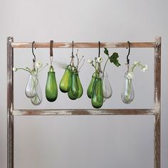 five green vases are hanging from a wooden rack with white flowers in each one