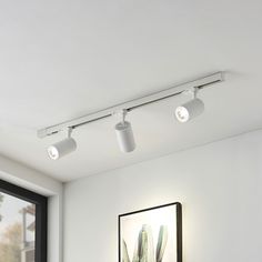 three lights are on the ceiling above a bed in a room with white walls and windows