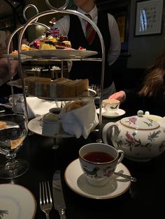 a table topped with plates and cups filled with desserts next to tea kettles