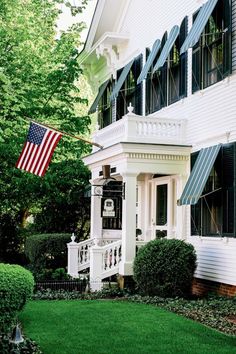 an american flag flying in front of a white house with black shutters and green grass