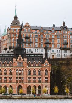 an old brick building sitting on the side of a river next to tall buildings with green spires