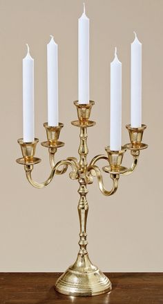 a gold candelabra with five white candles in it on a wooden table