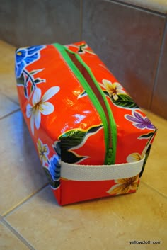 an orange flowered bag sitting on the floor next to a tile wall and counter