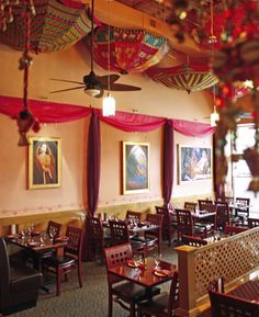 the interior of a restaurant with tables and chairs covered in red drapes, paintings on the wall