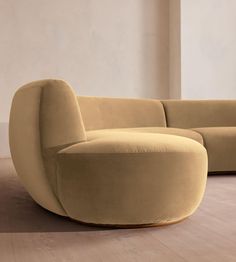 a curved couch sitting on top of a hard wood floor next to a white wall