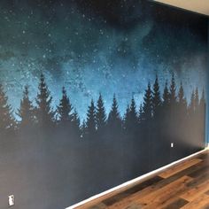 an empty room with wood flooring and painted trees on the wall in front of it