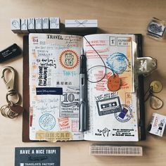 an open notebook with stamps, keys and other items surrounding it on a wooden table