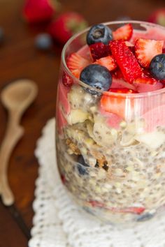 a jar filled with fruit and cereal on top of a wooden table next to a spoon