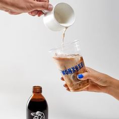 two people are pouring something into a drink in a glass and another person is holding a beer bottle