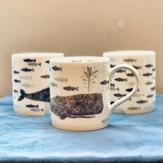 three coffee mugs with fish on them sitting on a blue towel next to each other