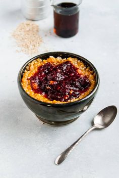 a bowl filled with oatmeal and jam next to two spoons on a table