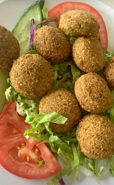 a white plate topped with meatballs and lettuce next to a slice of tomato