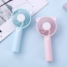 two small portable fans sitting next to each other on a blue and pink table top