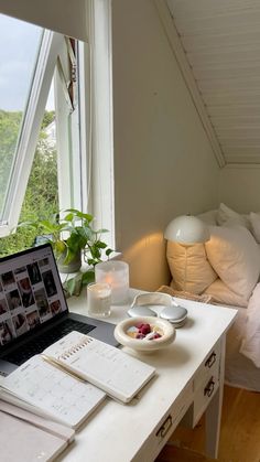 an open laptop computer sitting on top of a white desk next to a bowl of fruit