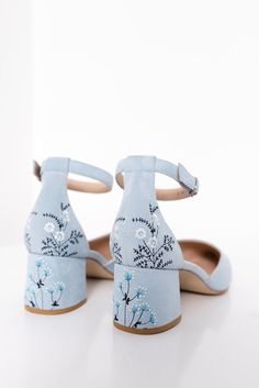 a pair of blue shoes with flowers painted on the front and back, sitting on a white surface