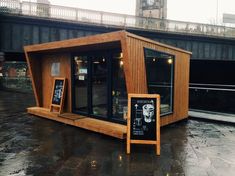 a small wooden structure sitting on top of a wet ground next to a clock tower