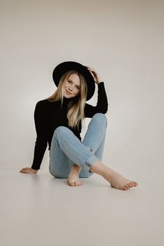 a woman sitting on the floor wearing jeans and a black hat