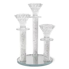 three glass candlesticks and one candle holder are on a stand with silver glitter