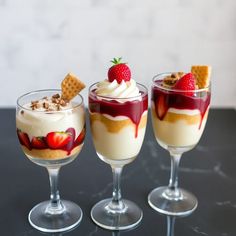 three desserts with strawberries and whipped cream in small glasses on a black table