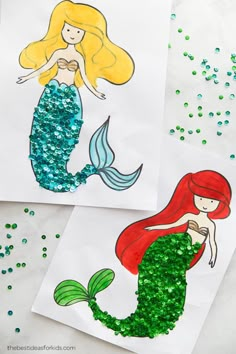 two little mermaids made out of paper with green glitter on the bottom and one is holding